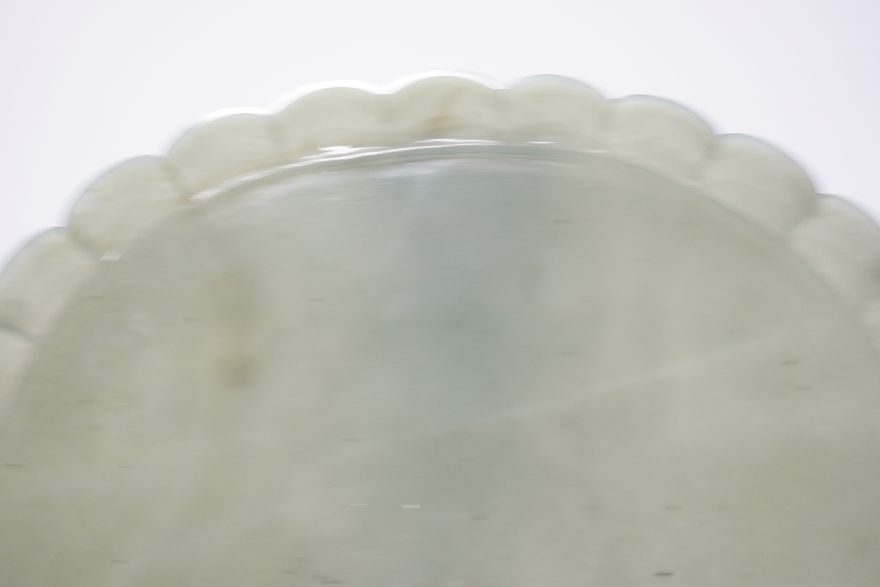 A Mughal style oval celadon jade dish, with petal lobed rim the underside carved with leaves, wood stand, 20cm